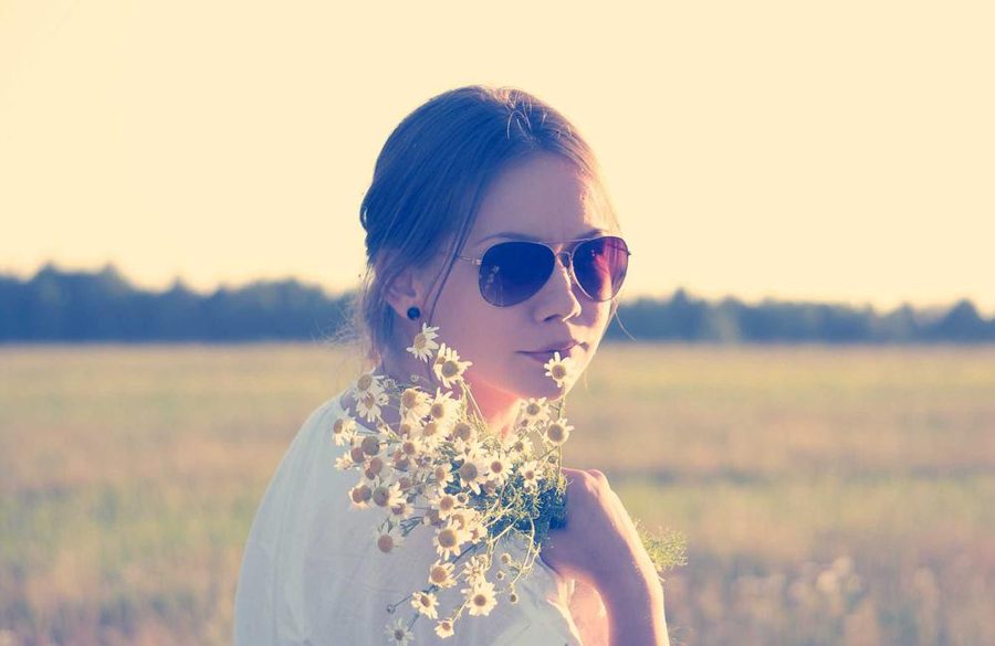 A woman in sunglasses holding a bunch of daisies in a sunny field